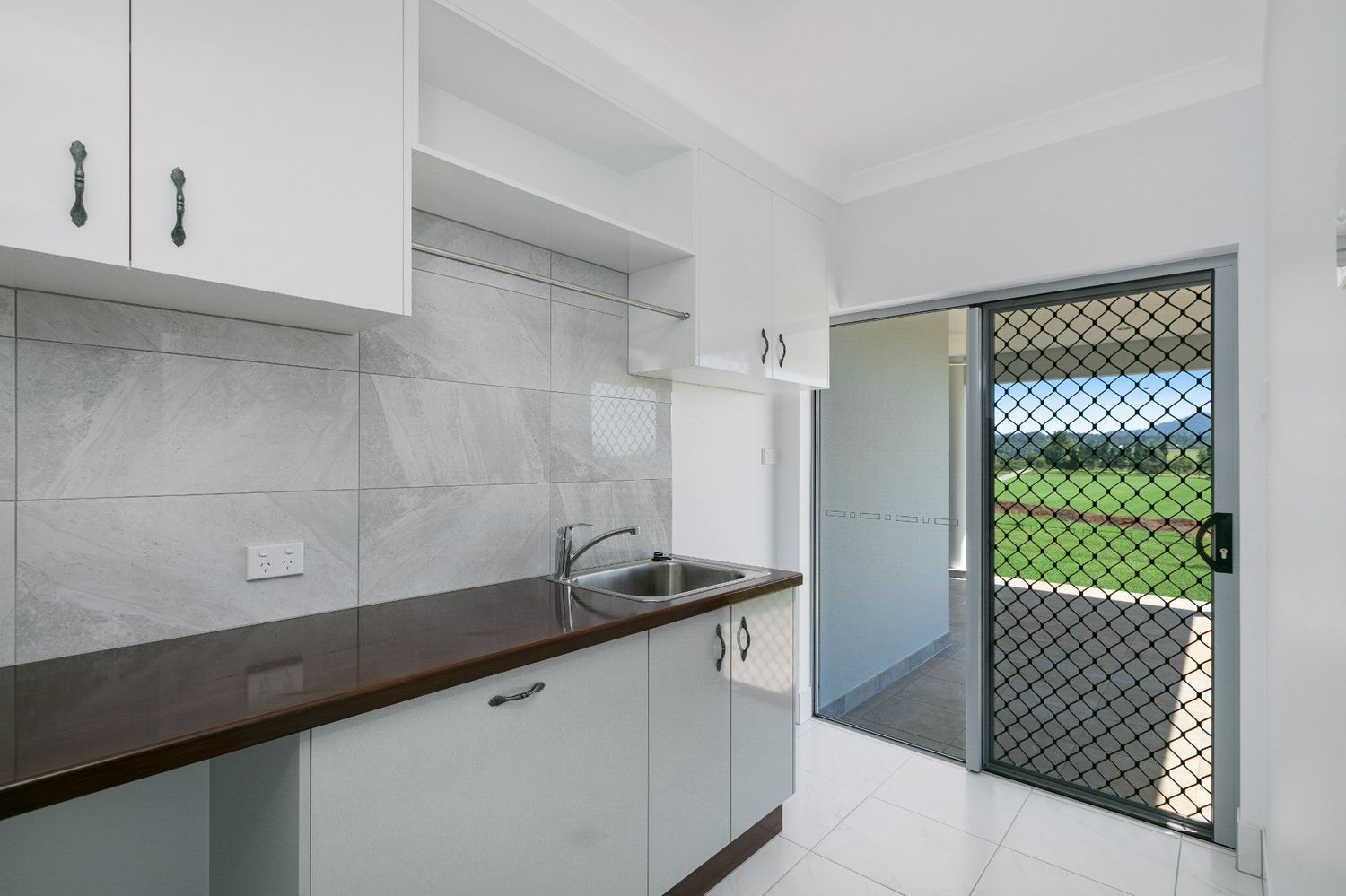 An Empty Kitchen With White Cabinets, a Sink, and a Screen Door — Ashlee Jones Homes in Gordonvale, QLD