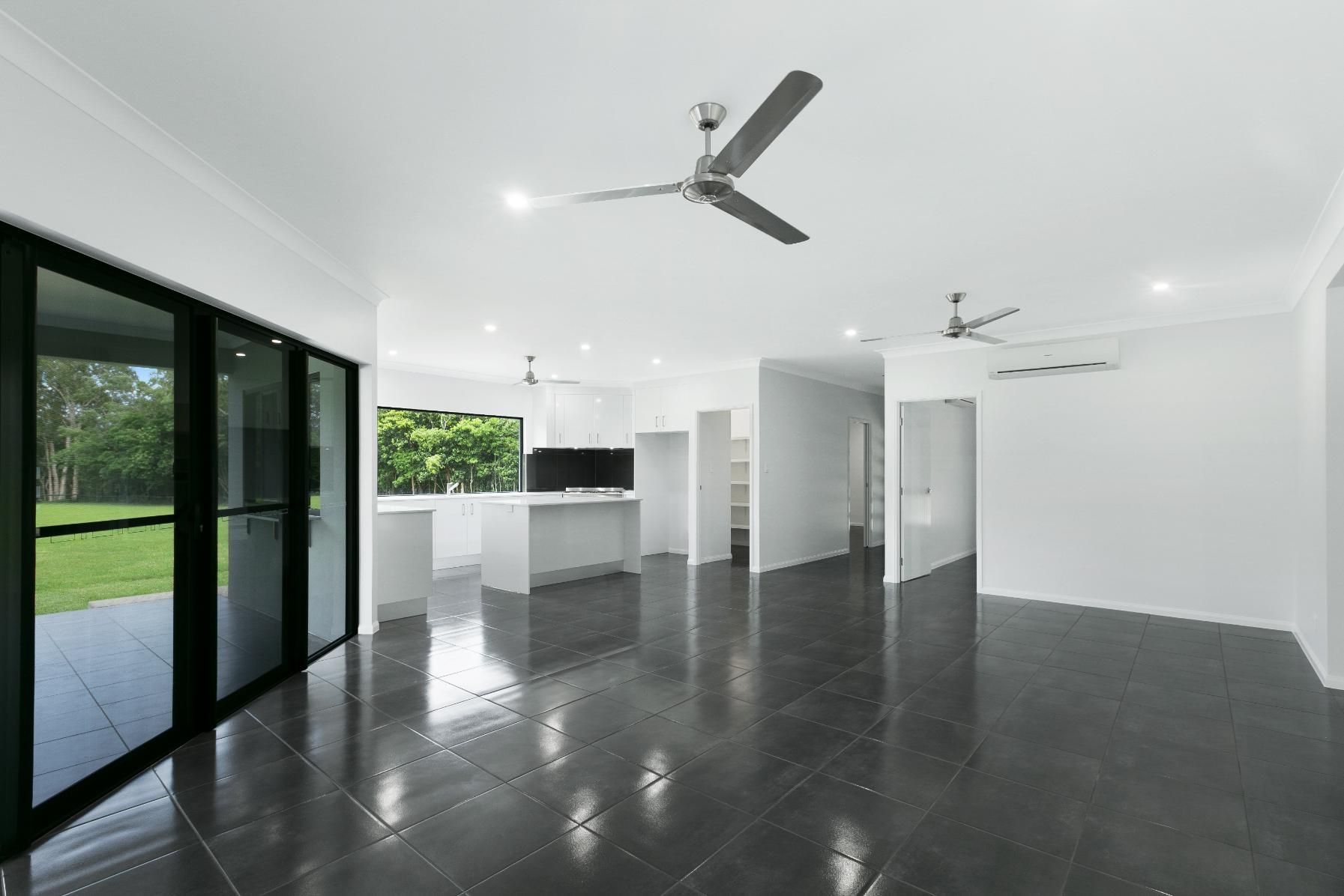 An Empty Living Room With a Ceiling Fan and Sliding Glass Doors — Ashlee Jones Homes in Gordonvale, QLD