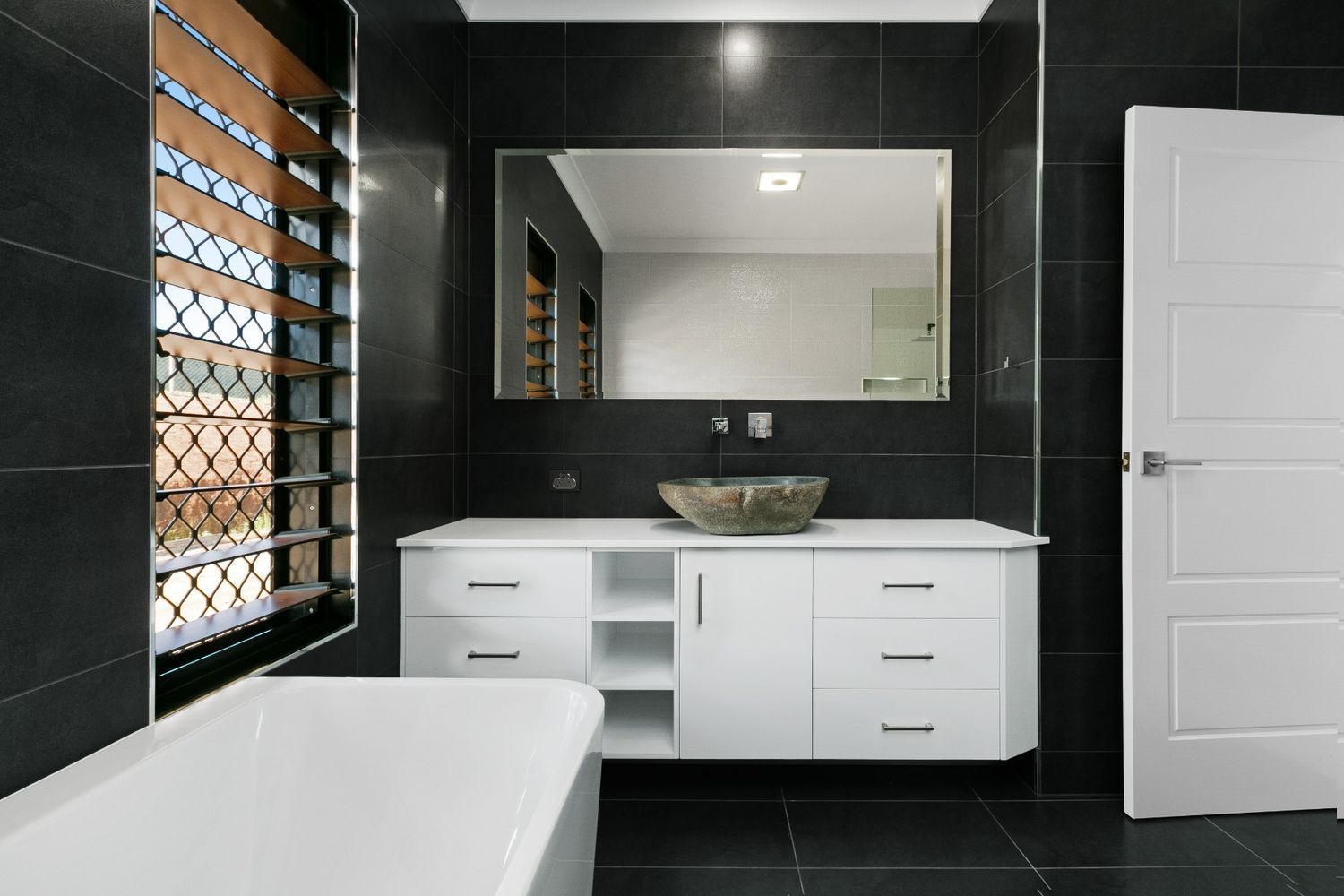A Bathroom With Black Tiles and White Cabinets and a Sink — Ashlee Jones Homes in Gordonvale, QLD