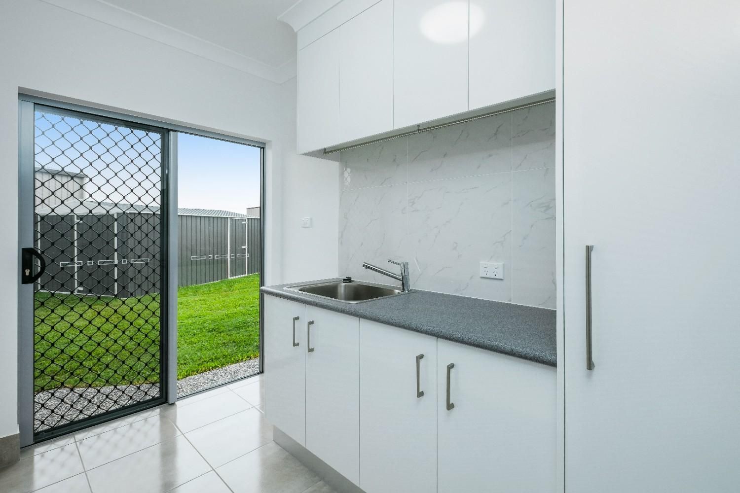 A Kitchen With White Cabinets, a Sink, and a Sliding Glass Door — Ashlee Jones Homes in Gordonvale, QLD
