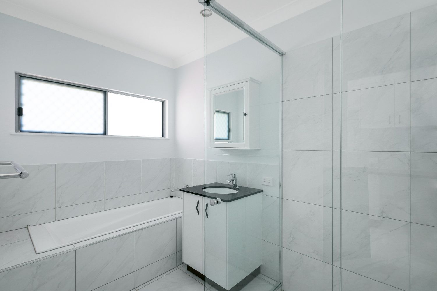 A Bathroom With a Sink and a Bathtub With a Glass Shower Door — Ashlee Jones Homes in Gordonvale, QLD