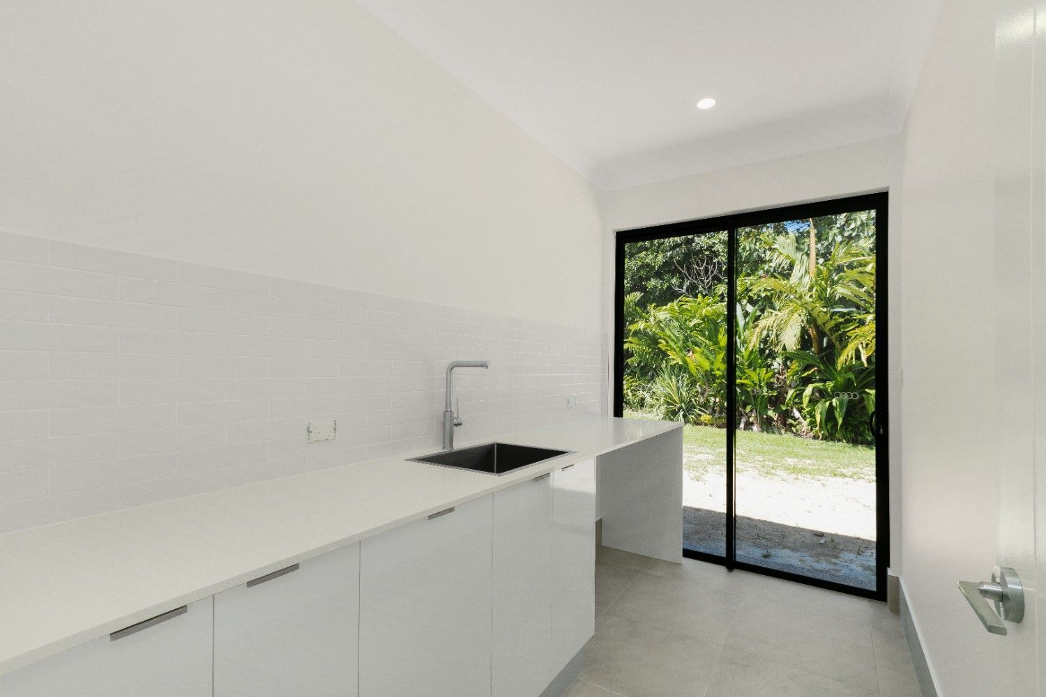 A Kitchen With White Cabinets, a Sink, and a Sliding Glass Door — Ashlee Jones Homes in Gordonvale, QLD