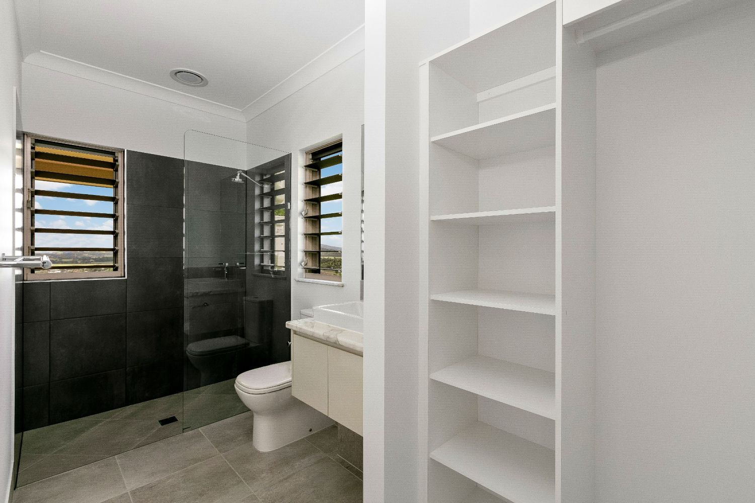 A Bathroom With a Toilet, Sink, Shower and Shelves — Ashlee Jones Homes in Gordonvale, QLD