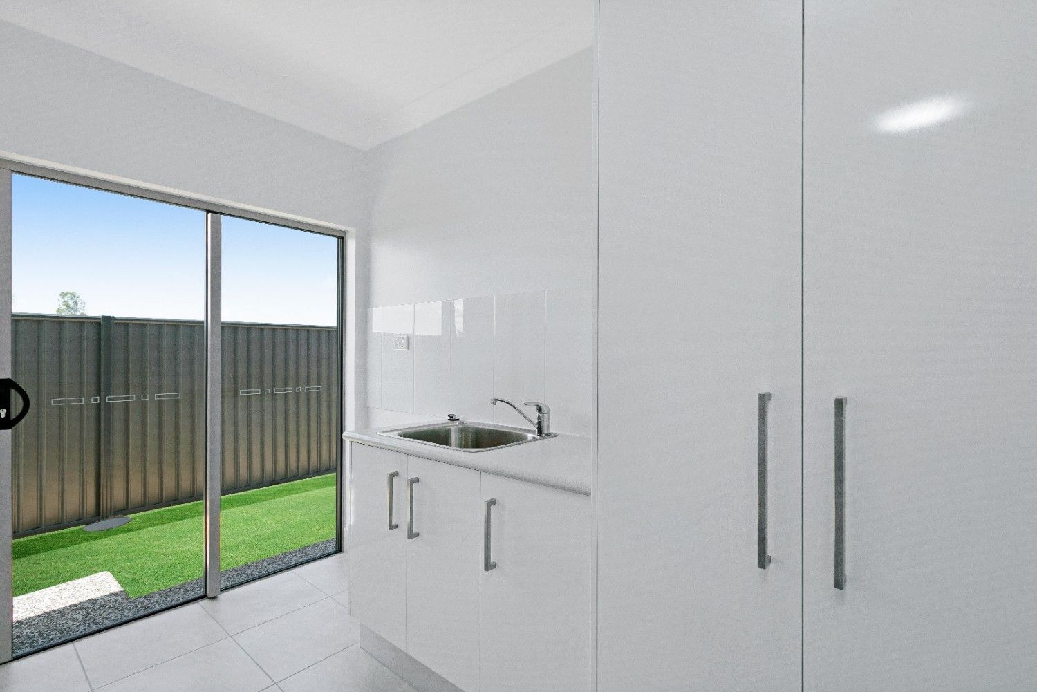 A Laundry Room With White Cabinets, a Sink, and a Sliding Glass Door — Ashlee Jones Homes in Gordonvale, QLD
