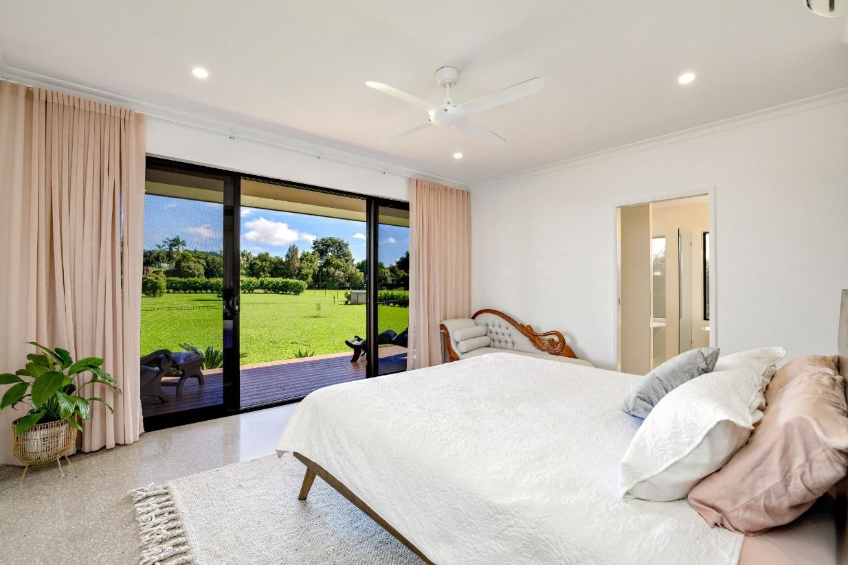 A Bedroom With a Large Bed and Sliding Glass Doors Leading to a Patio — Ashlee Jones Homes in Gordonvale, QLD