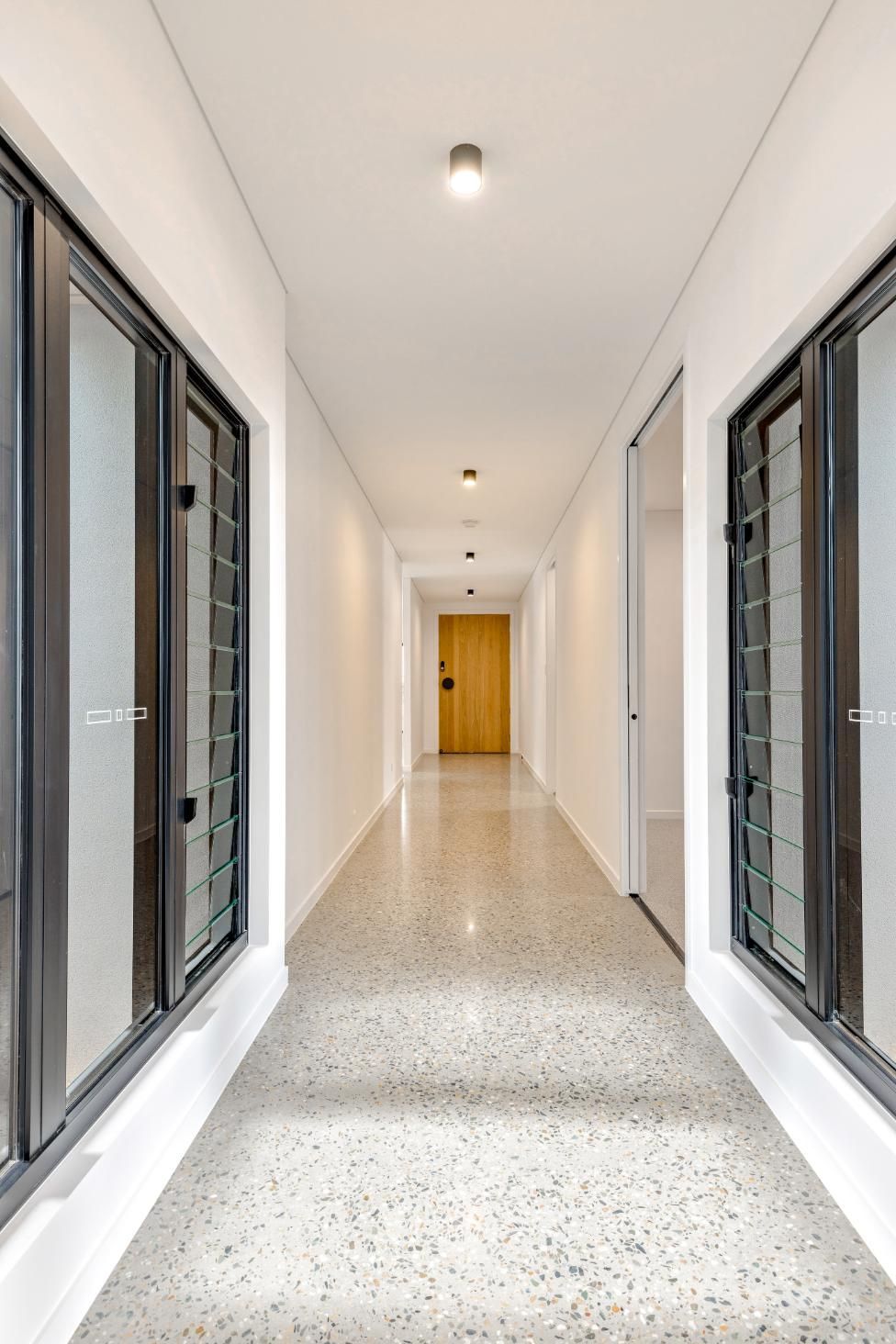 A Long Hallway with A Wooden Door and A Lot of Windows — Ashlee Jones Homes in Gordonvale, QLD