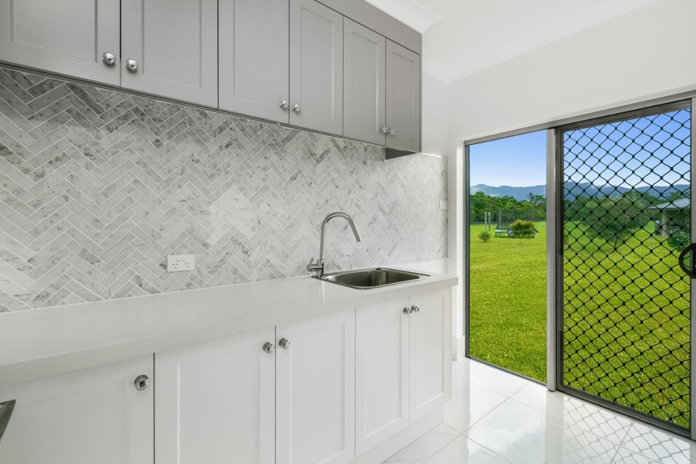 A Kitchen With White Cabinets, a Sink, and a Sliding Glass Door — Ashlee Jones Homes in Gordonvale, QLD
