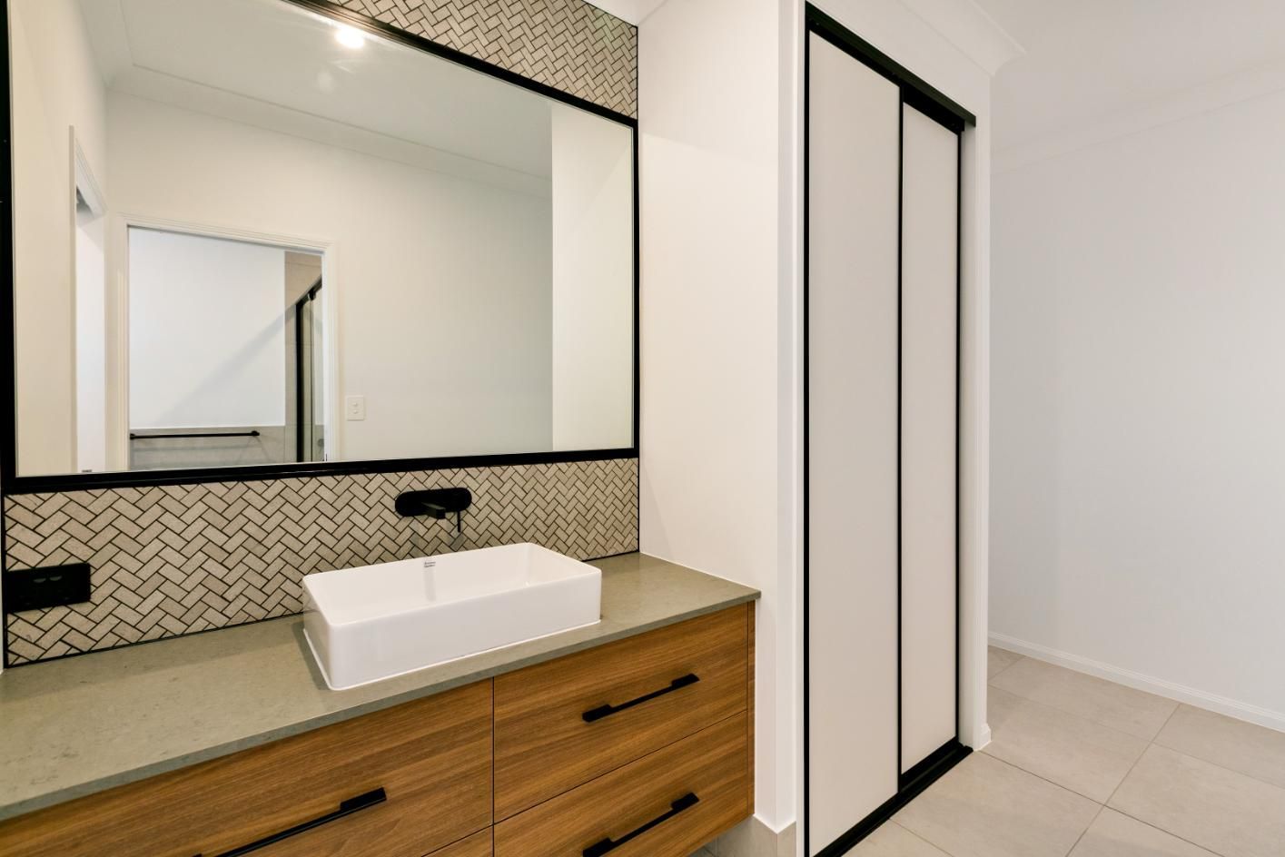 A Bathroom With a Sink, Mirror and Sliding Glass Door — Ashlee Jones Homes in Gordonvale, QLD