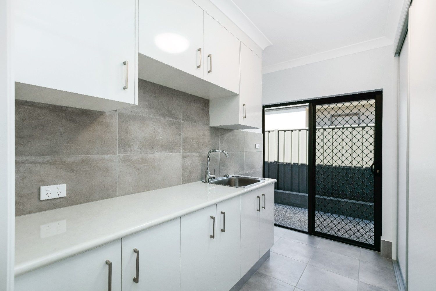 A Kitchen With White Cabinets and a Sliding Glass Door — Ashlee Jones Homes in Gordonvale, QLD