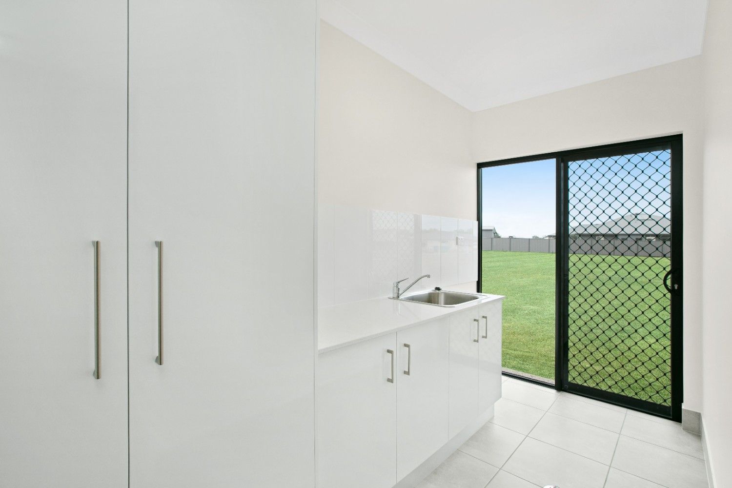 A Laundry Room With White Cabinets and a Sliding Glass Door — Ashlee Jones Homes in Gordonvale, QLD
