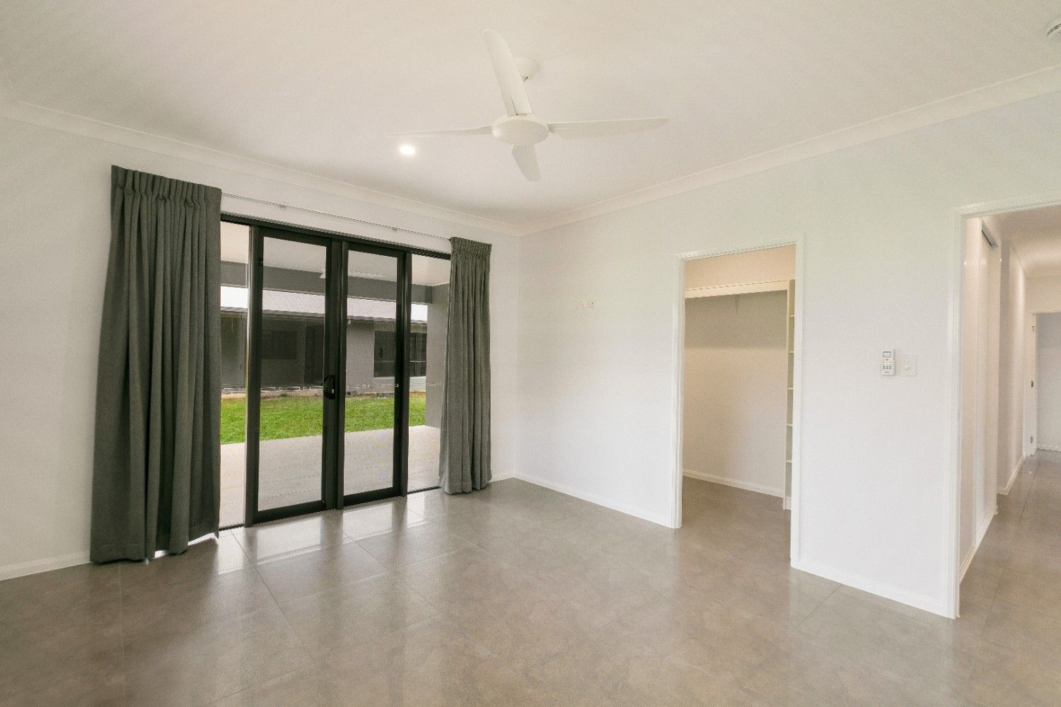 An Empty Living Room With Sliding Glass Doors and a Ceiling Fan — Ashlee Jones Homes in Gordonvale, QLD