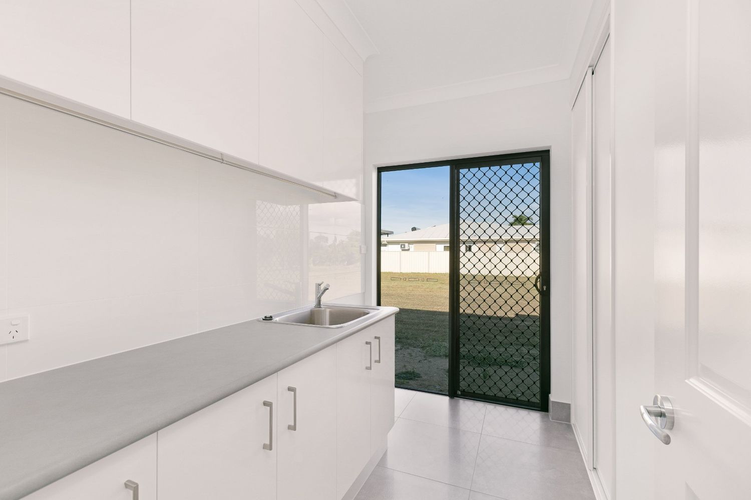 A Kitchen With White Cabinets, a Sink, and a Sliding Glass Door — Ashlee Jones Homes in Gordonvale, QLD