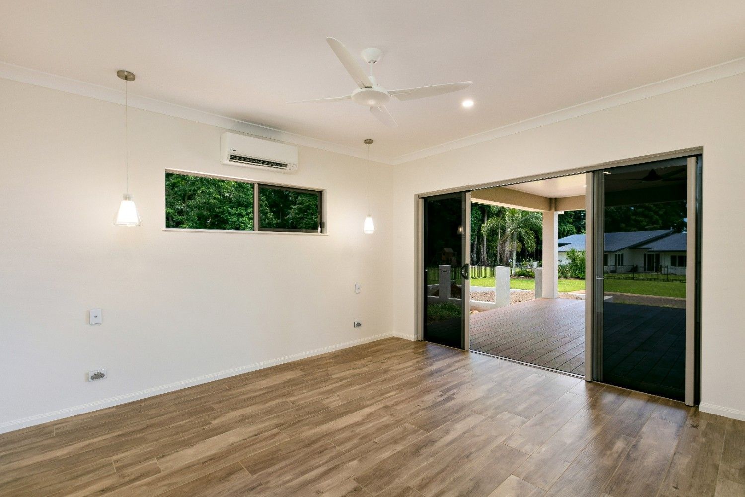 An Empty Living Room With Hardwood Floors and a Ceiling Fan — Ashlee Jones Homes in Gordonvale, QLD