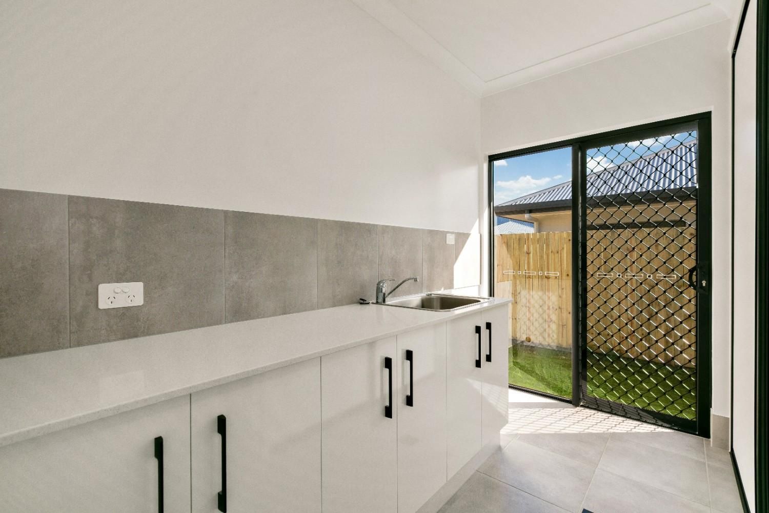 A Kitchen With White Cabinets, a Sink, and a Sliding Glass Door  — Ashlee Jones Homes in Gordonvale, QLD