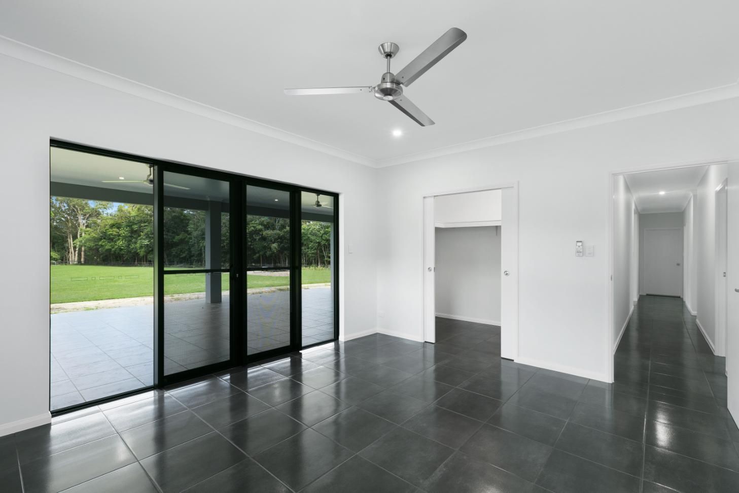 An Empty Living Room With a Ceiling Fan and Sliding Glass Doors — Ashlee Jones Homes in Gordonvale, QLD