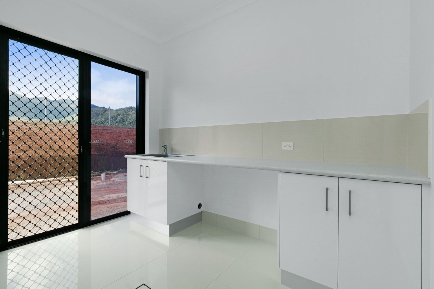 An Empty Kitchen With White Cabinets and Sliding Glass Doors — Ashlee Jones Homes in Gordonvale, QLD