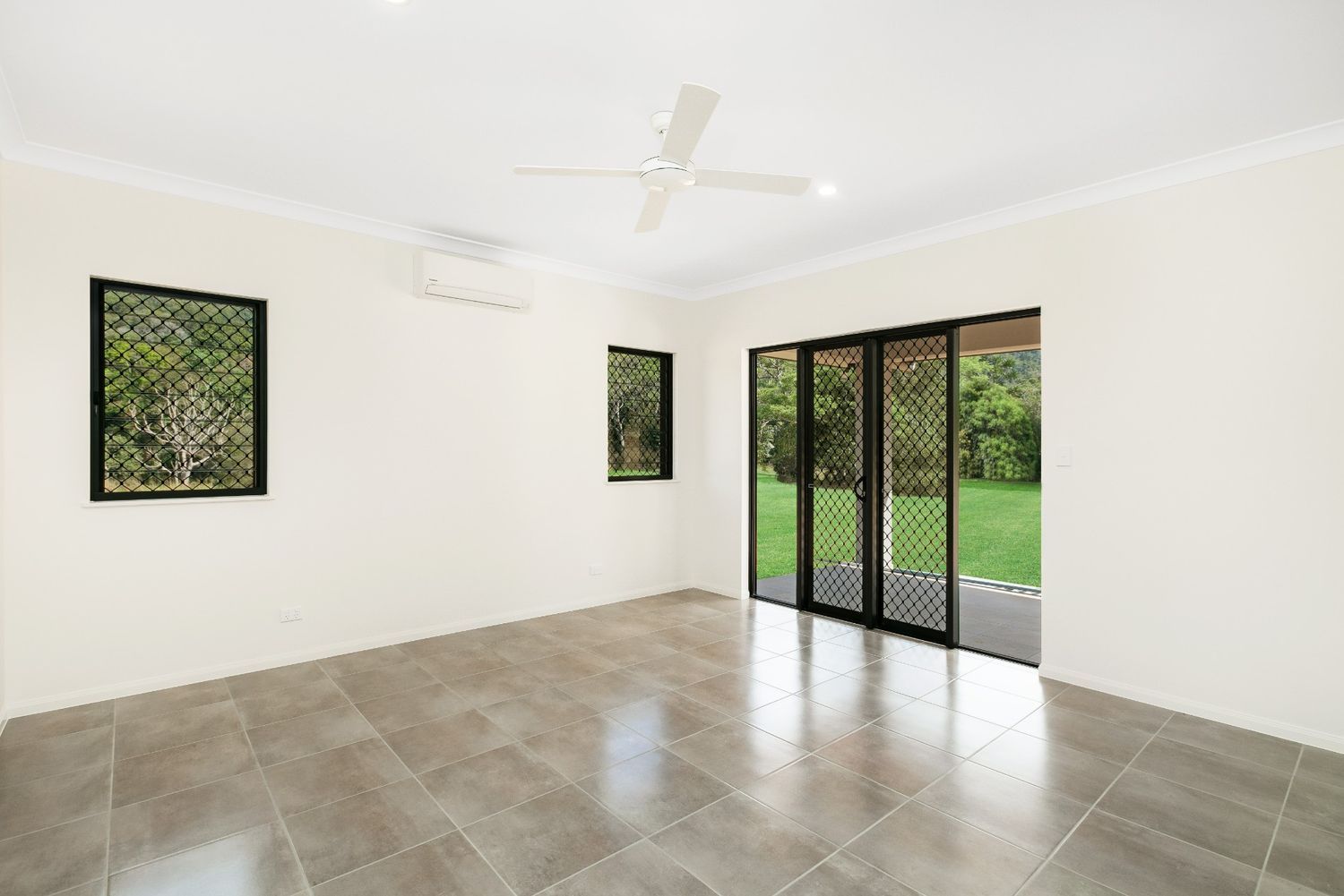 An Empty Living Room With Sliding Glass Doors and a Ceiling Fan — Ashlee Jones Homes in Gordonvale, QLD