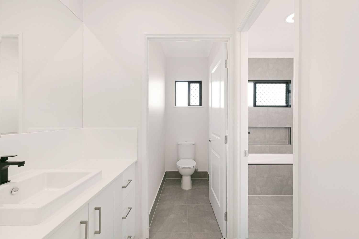 A Bathroom With a Toilet, Sink and Mirror — Ashlee Jones Homes in Gordonvale, QLD