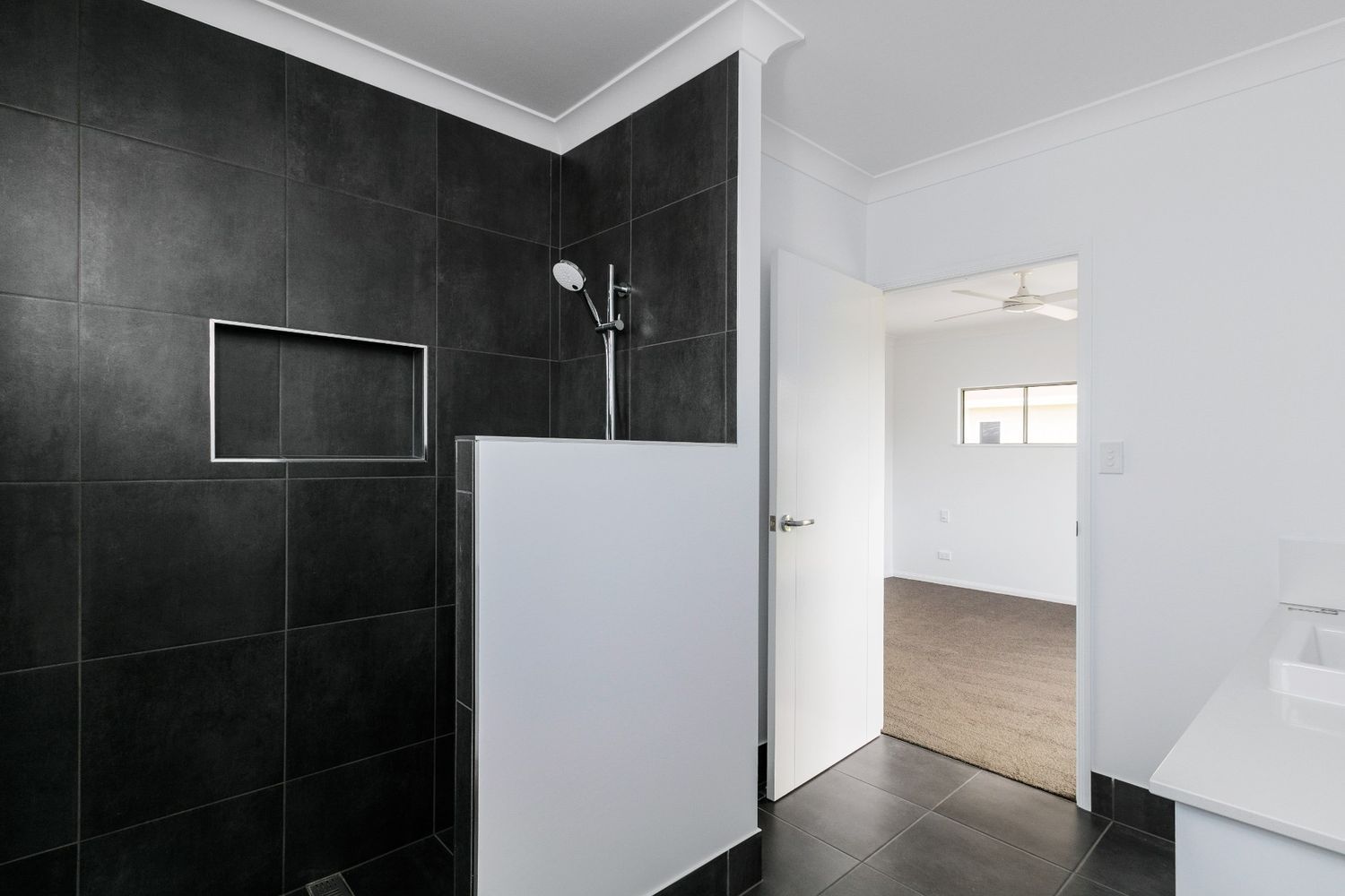 A Bathroom With Black Tiles and a Walk in Shower — Ashlee Jones Homes in Gordonvale, QLD