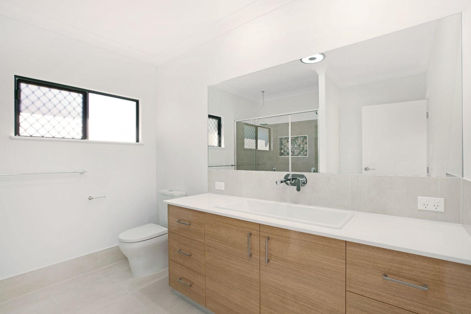 A Bathroom With a Toilet, Sink, Mirror and Window — Ashlee Jones Homes in Gordonvale, QLD