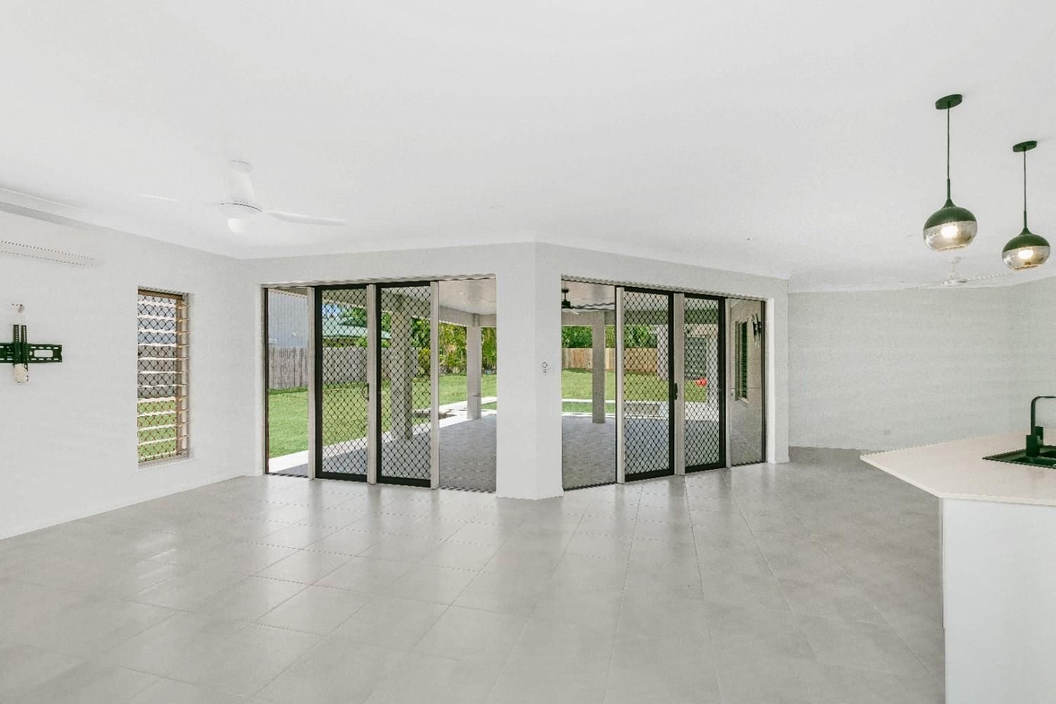 A Large Empty Room With Sliding Glass Doors and a Kitchen — Ashlee Jones Homes in Gordonvale, QLD