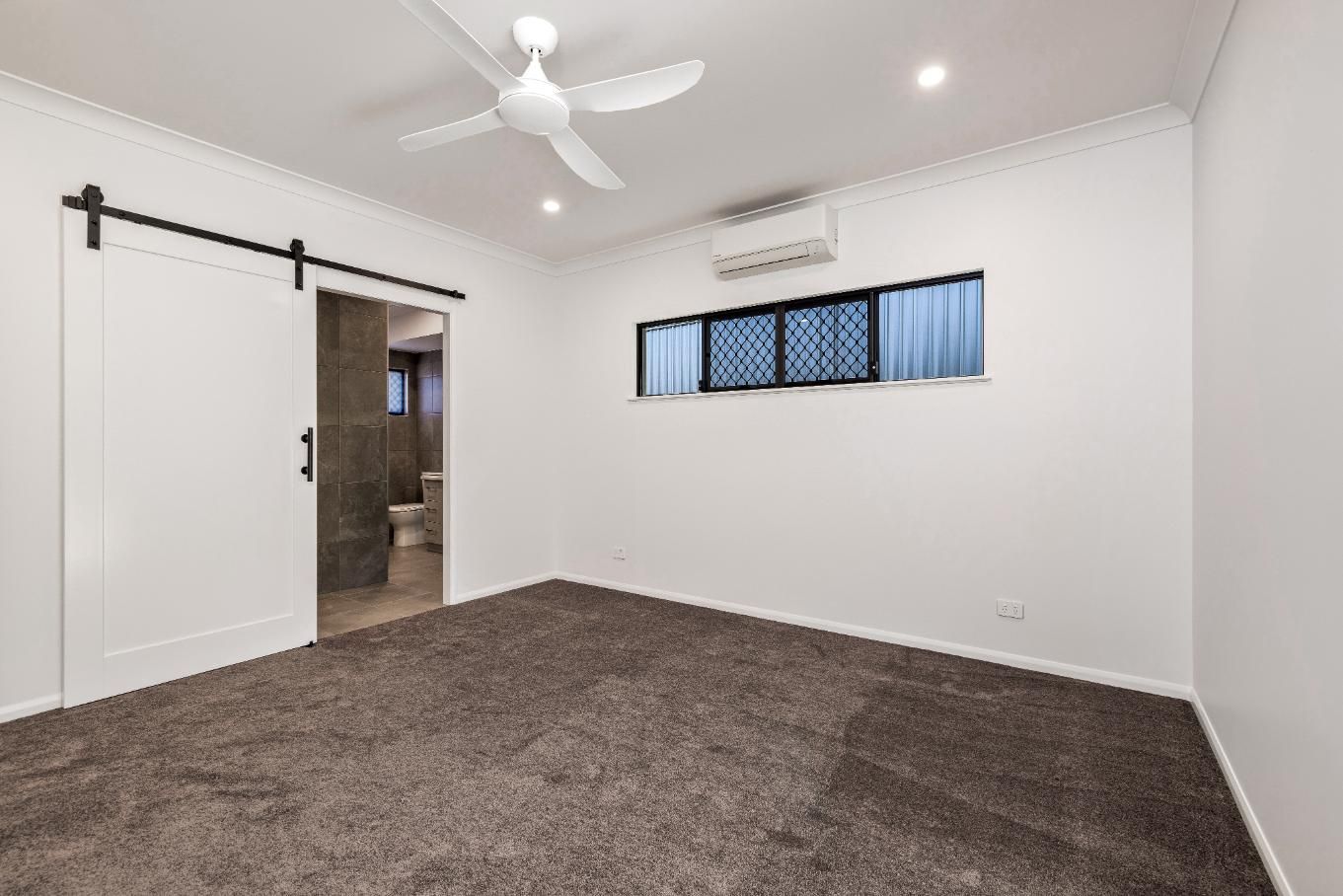 An Empty Bedroom With a Ceiling Fan and a Sliding Barn Door — Ashlee Jones Homes in Gordonvale, QLD
