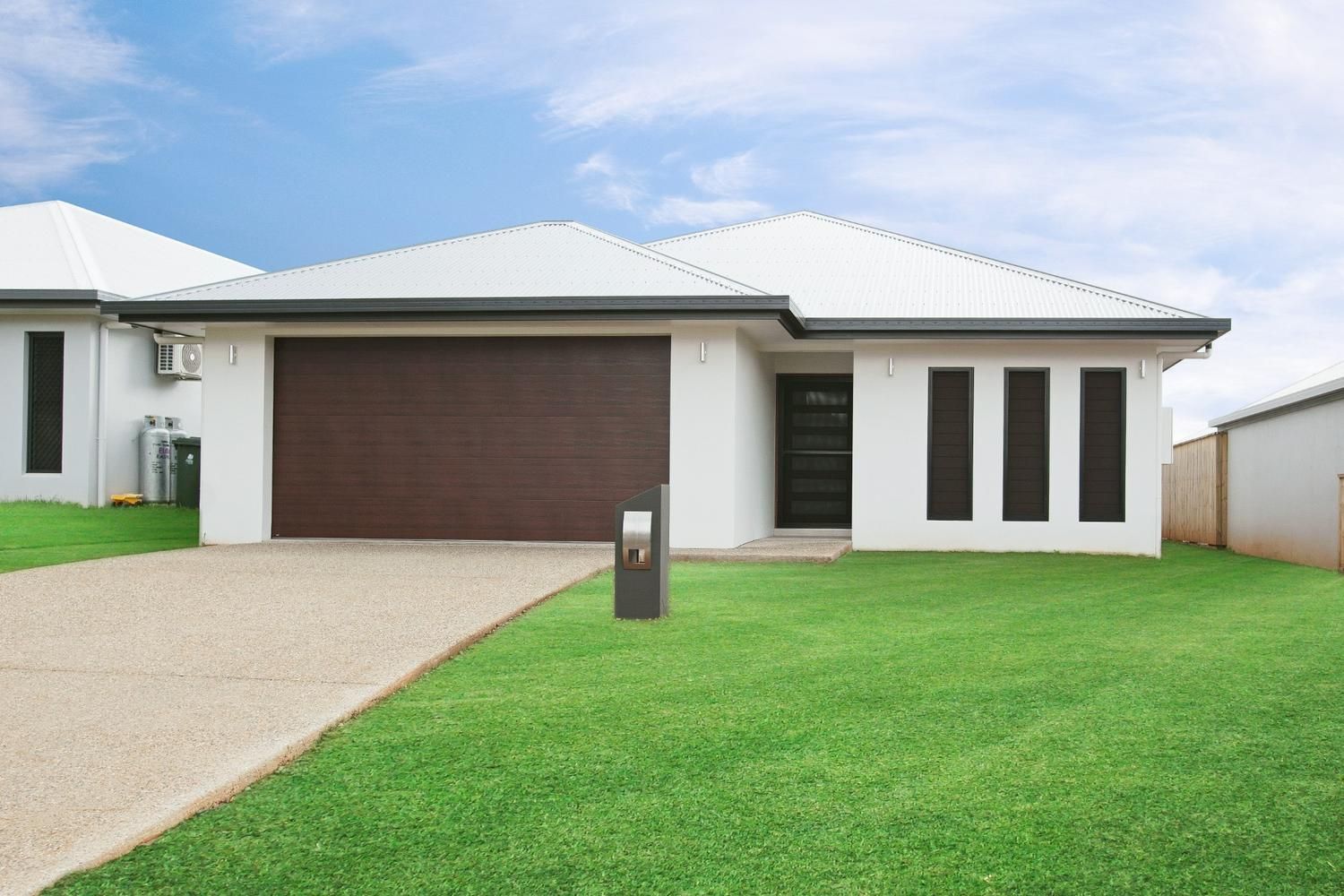 A White House With a Brown Garage Door is Sitting on Top of a Lush Green Lawn — Ashlee Jones Homes in Gordonvale, QLD