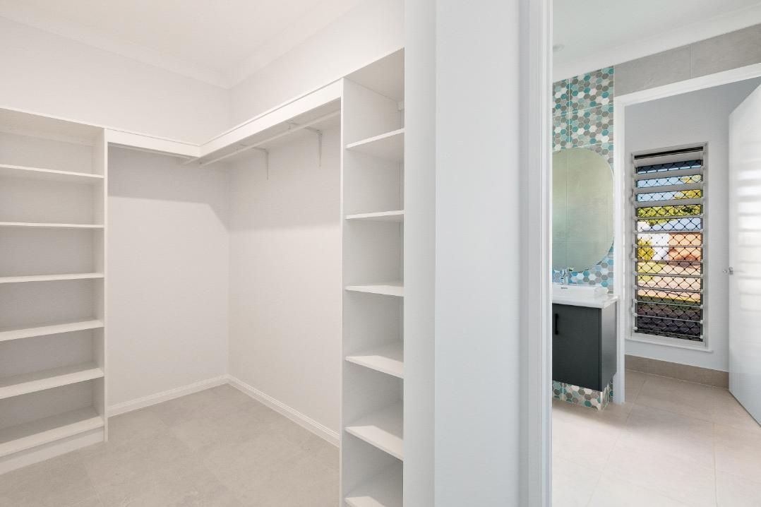 An Empty Walk in Closet With White Shelves and a Bathroom in the Background — Ashlee Jones Homes in Gordonvale, QLD