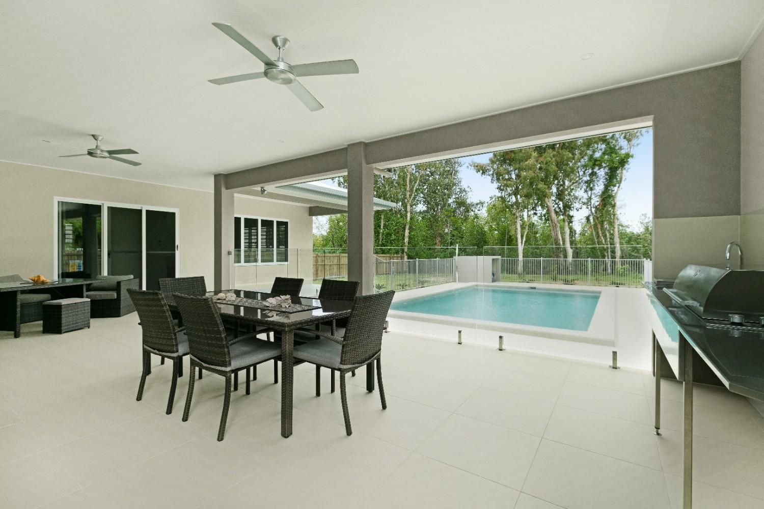 A Patio With a Table and Chairs and a Ceiling Fan Overlooking a Swimming Pool — Ashlee Jones Homes in Gordonvale, QLD