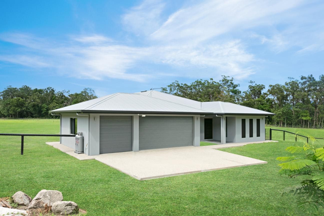A House With Two Garages is Sitting in the Middle of a Lush Green Field — Ashlee Jones Homes in Gordonvale, QLD
