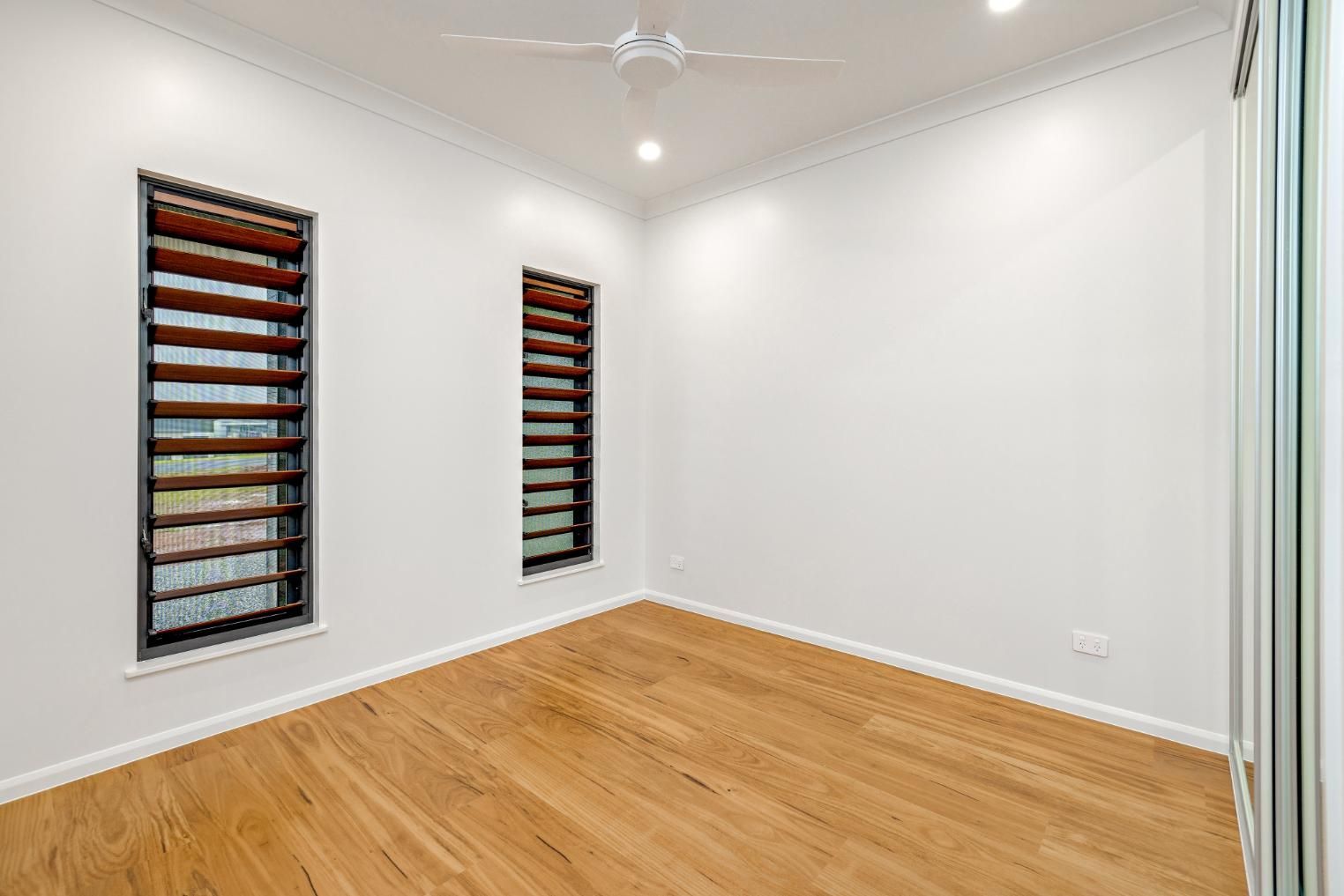 An Empty Room With Hardwood Floors and Two Windows — Ashlee Jones Homes in Gordonvale, QLD