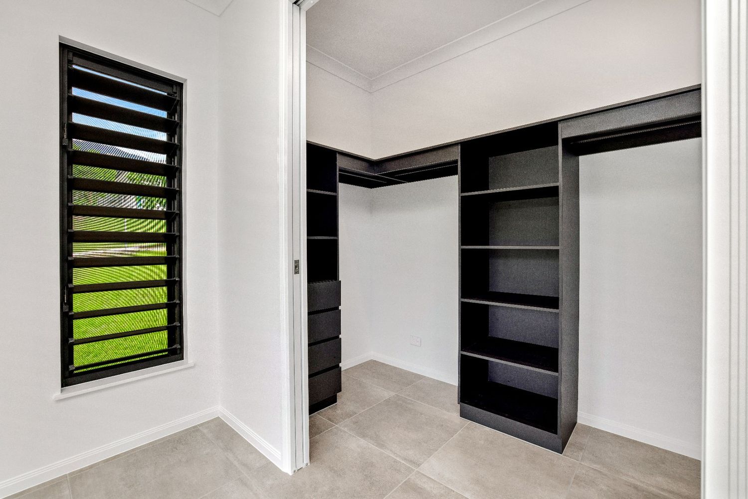 A Walk in Closet With Black Shelves and a Window — Ashlee Jones Homes in Gordonvale, QLD