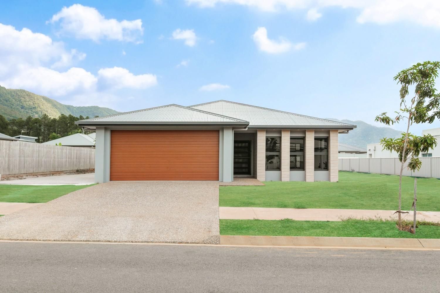 A House With a Brown Garage Door and Mountains in the Background — Ashlee Jones Homes in Gordonvale, QLD