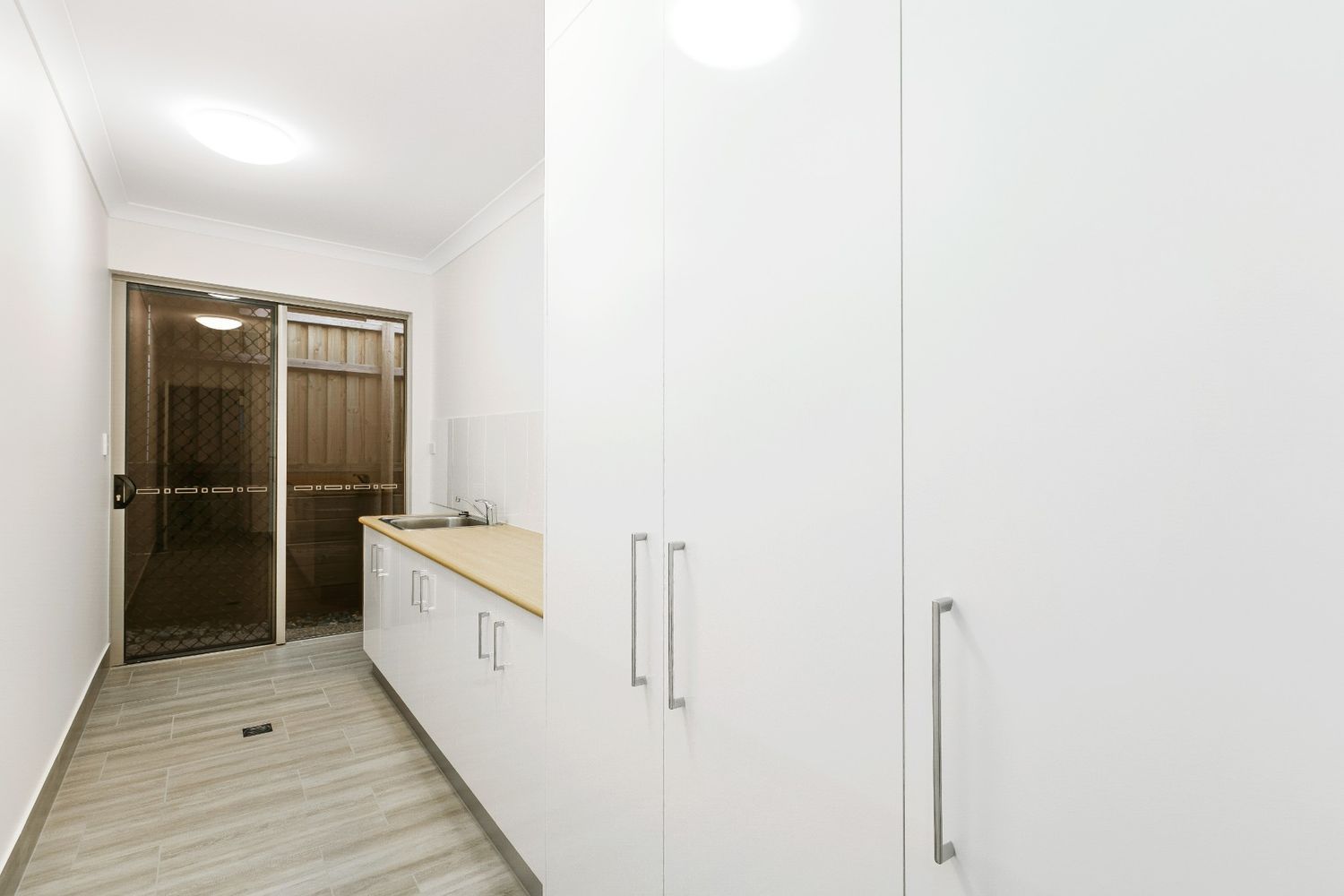 A Laundry Room With White Cabinets, a Sink, and a Sliding Glass Door — Ashlee Jones Homes in Gordonvale, QLD