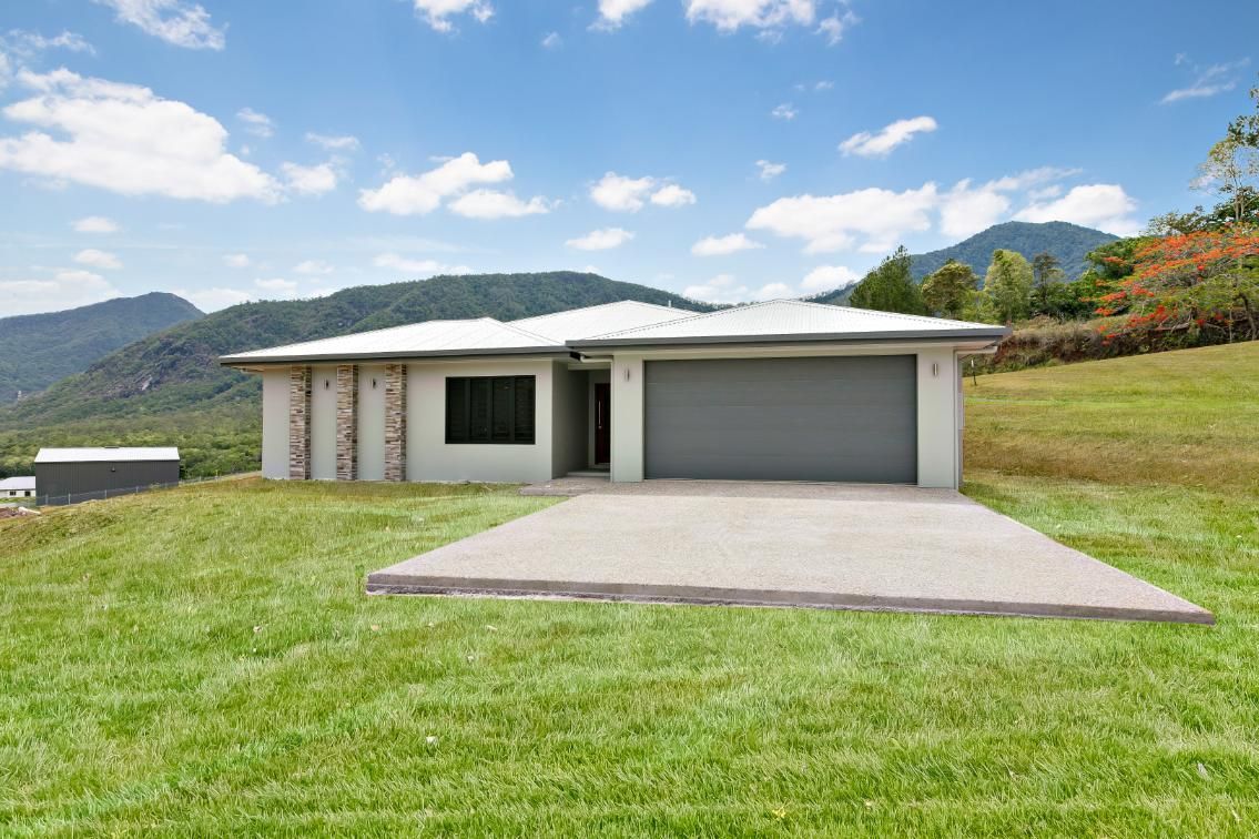 A House is Sitting on Top of a Lush Green Hillside With Mountains in the Background — Ashlee Jones Homes in Gordonvale, QLD