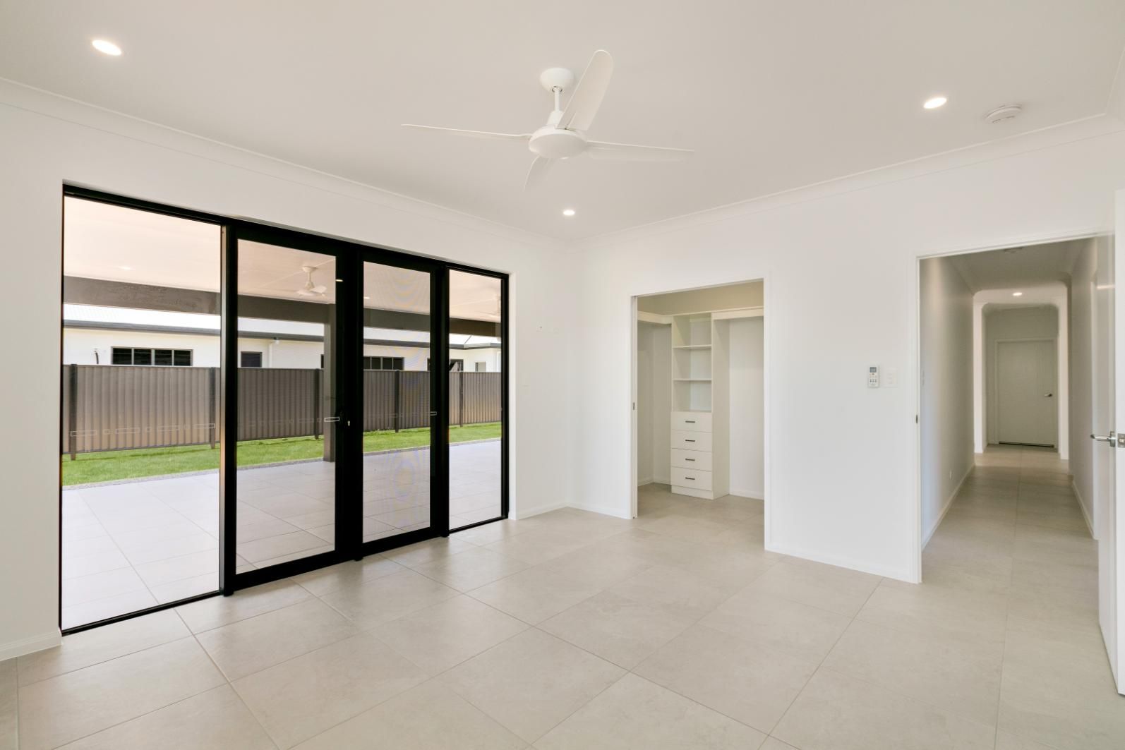 An Empty Living Room With Sliding Glass Doors and a Ceiling Fan — Ashlee Jones Homes in Gordonvale, QLD