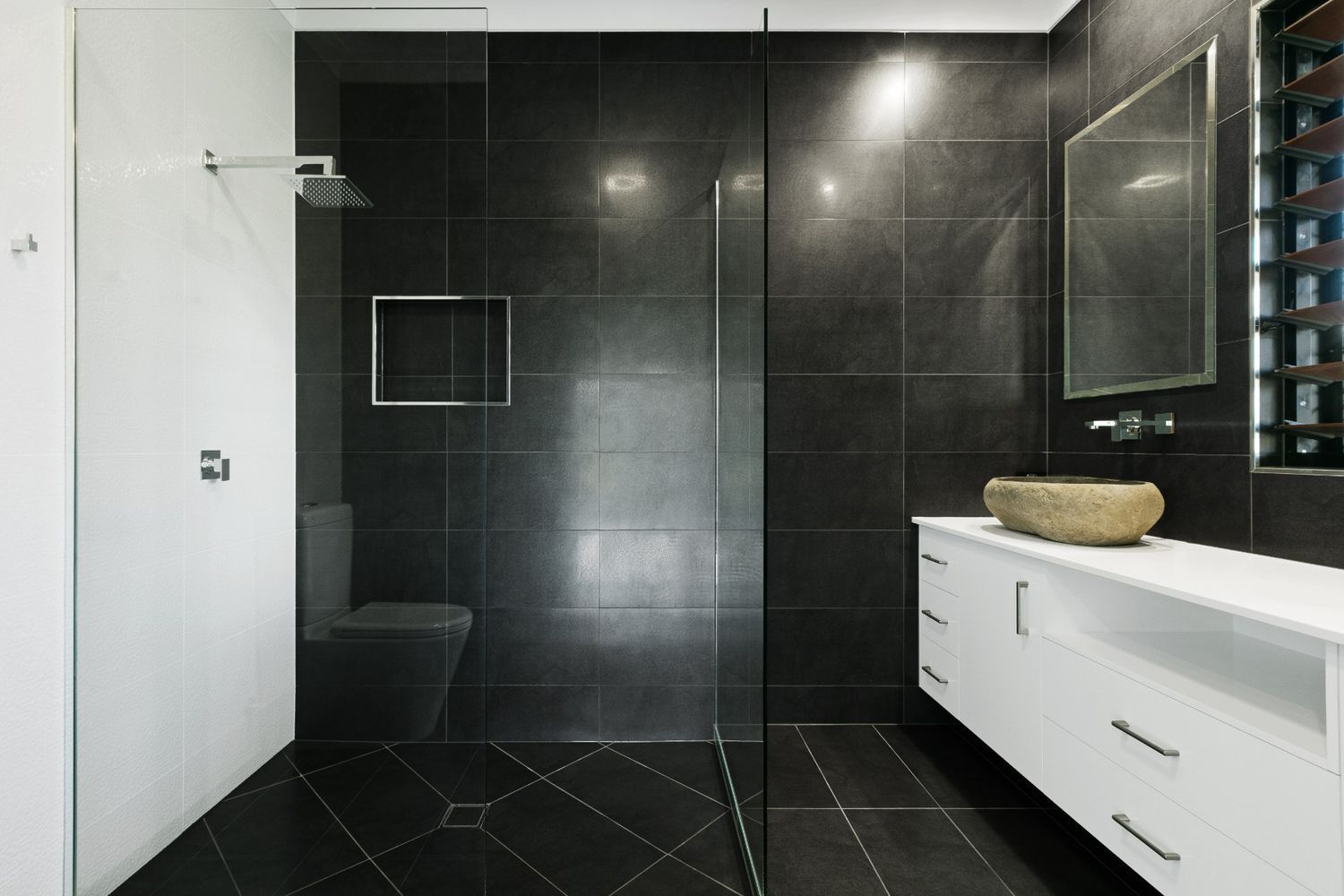 A Bathroom With Black Tiles and a Walk in Shower — Ashlee Jones Homes in Gordonvale, QLD