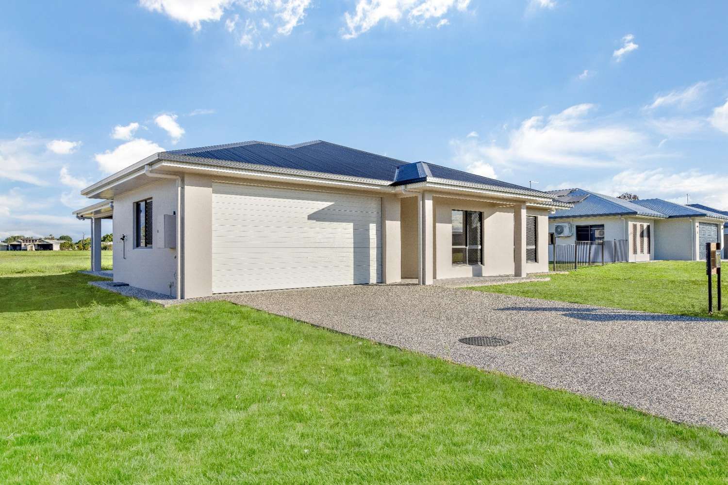 A House With a Garage is Sitting on Top of a Lush Green Field — Ashlee Jones Homes in Gordonvale, QLD