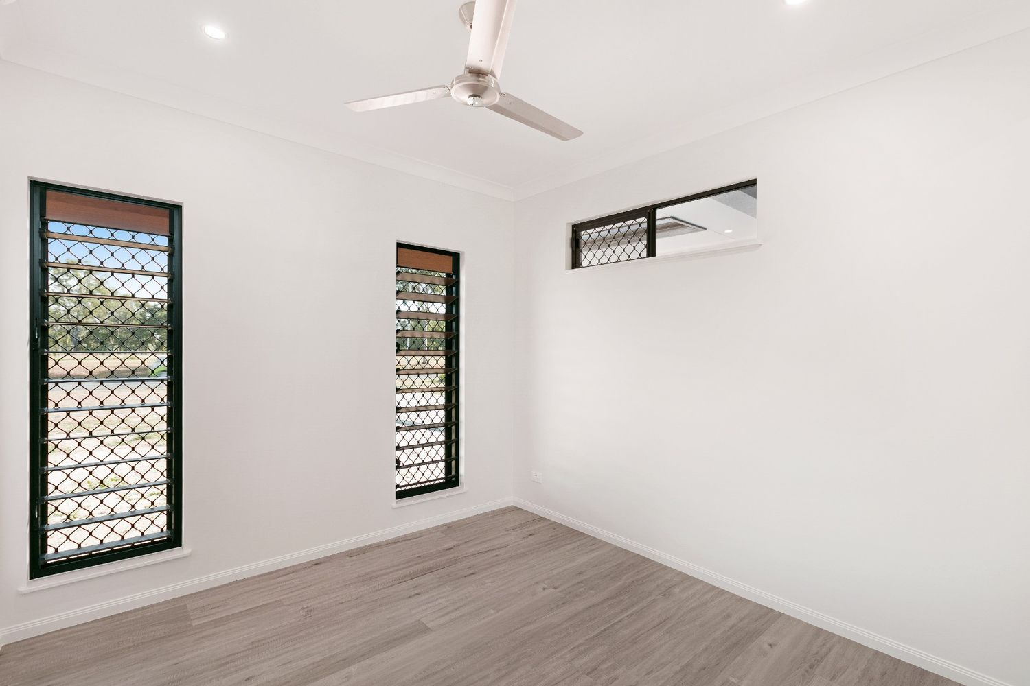 An Empty Room With Two Windows and a Ceiling Fan — Ashlee Jones Homes in Gordonvale, QLD
