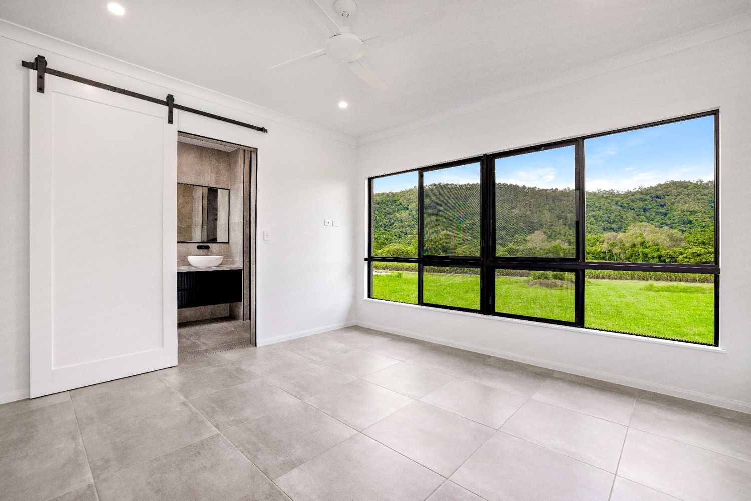 An Empty Room With a Sliding Barn Door and Large Windows — Ashlee Jones Homes in Gordonvale, QLD