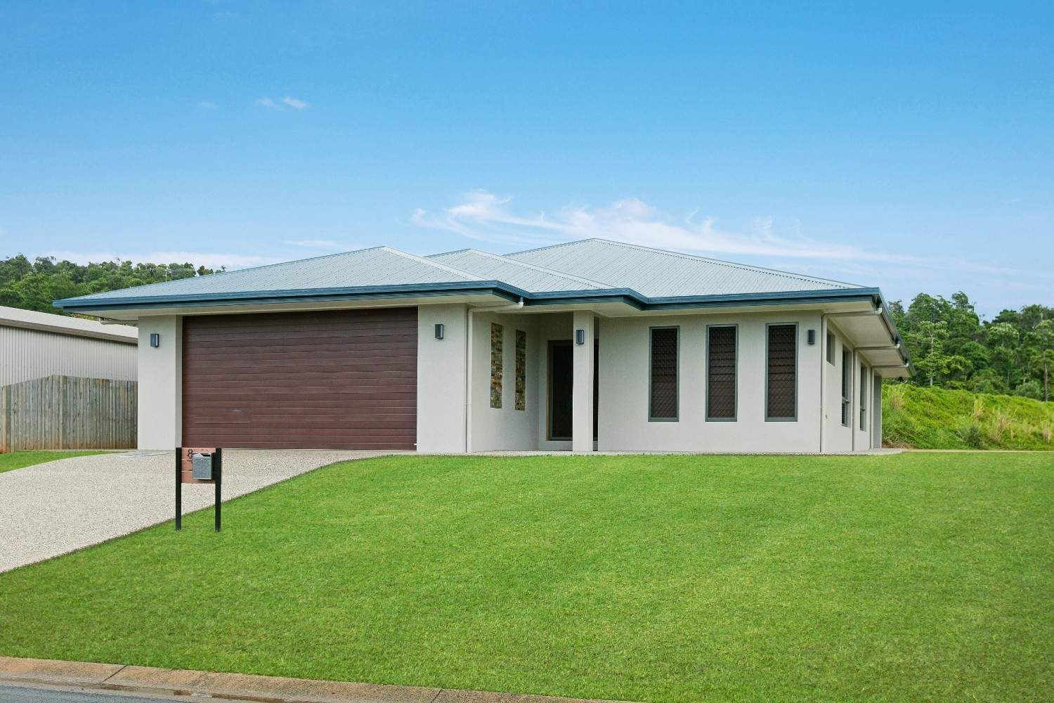 A House With a Brown Garage Door is Sitting on Top of a Lush Green Lawn — Ashlee Jones Homes in Gordonvale, QLD