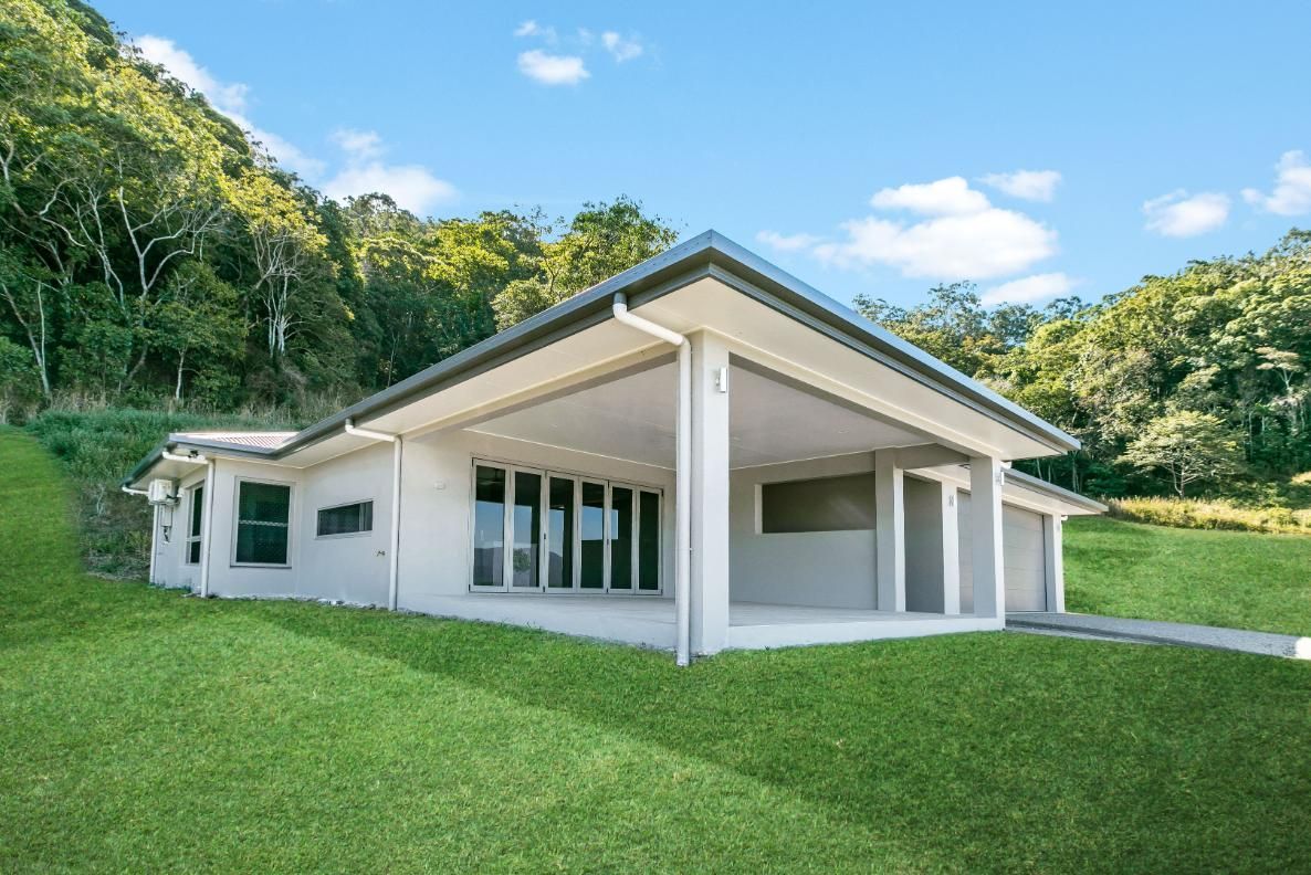 A White House is Sitting on Top of a Lush Green Hillside Surrounded by Trees — Ashlee Jones Homes in Gordonvale, QLD