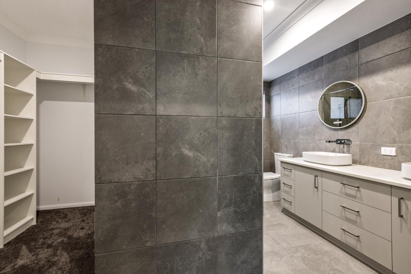 A Bathroom With a Walk in Closet, Sink, Toilet and Mirror — Ashlee Jones Homes in Gordonvale, QLD