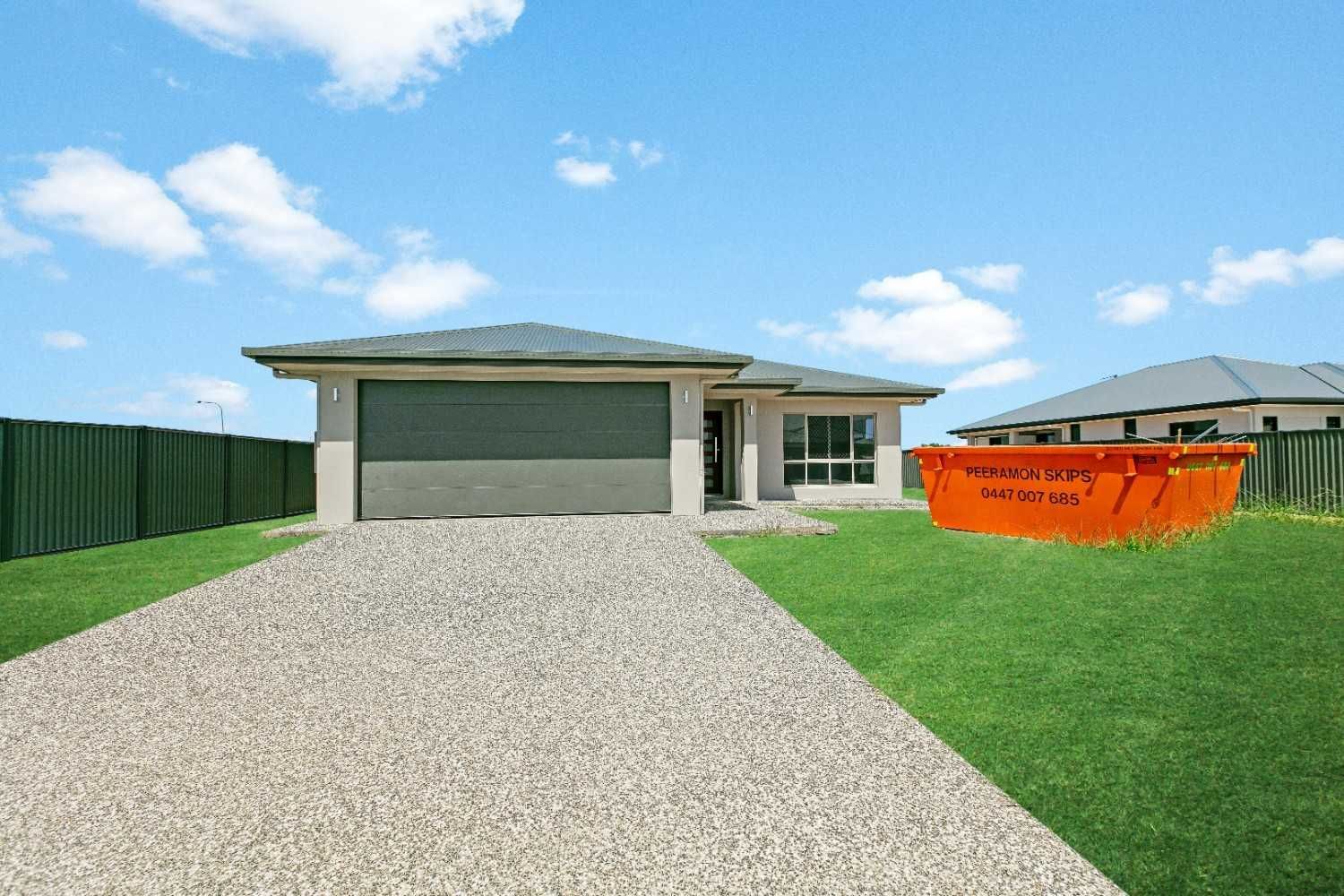 A White House With a Brown Garage Door is Sitting on Top of a Lush Green Lawn — Ashlee Jones Homes in Gordonvale, QLD