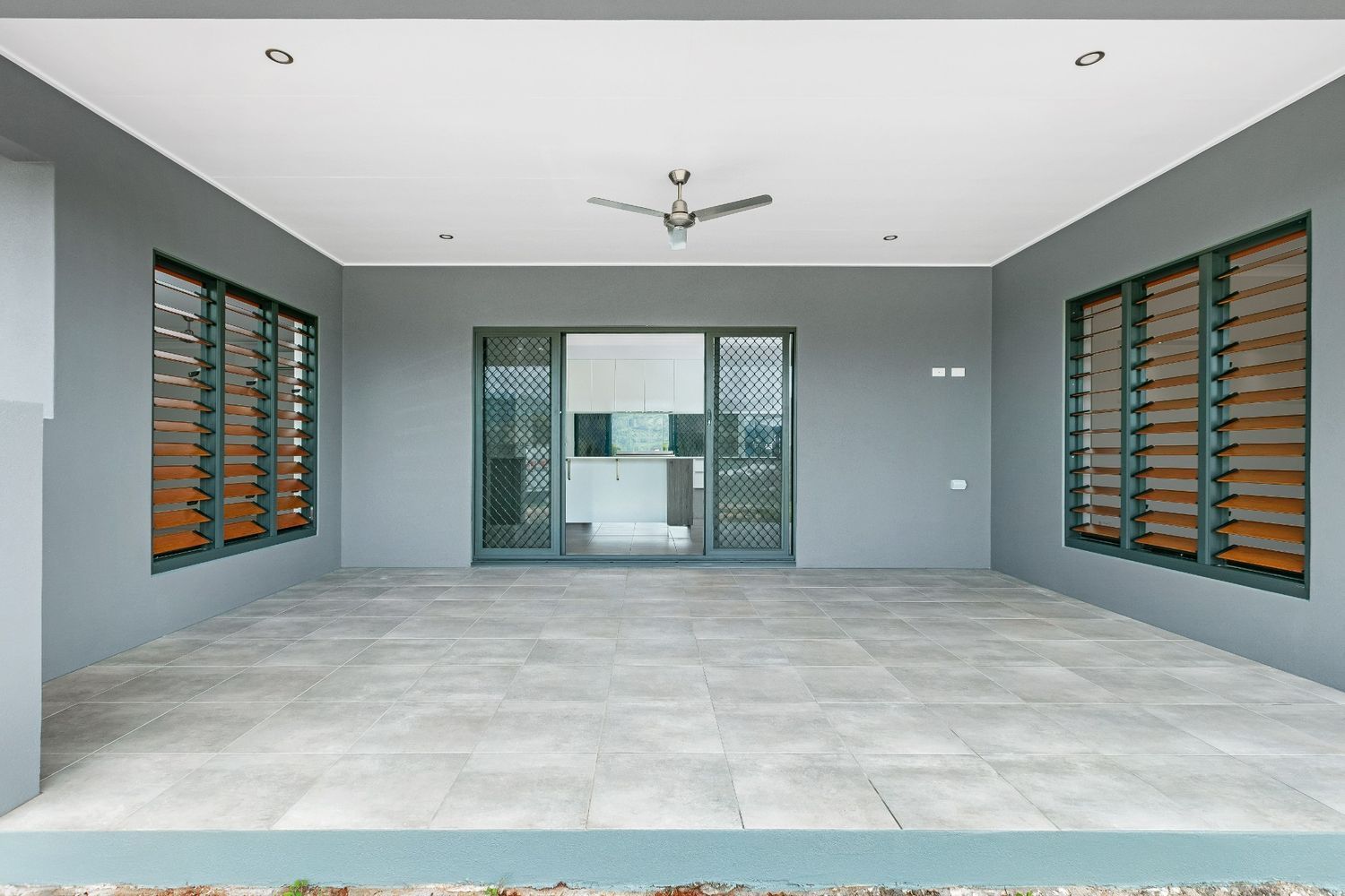 A Large Empty Room With a Ceiling Fan and Sliding Glass Doors — Ashlee Jones Homes in Gordonvale, QLD