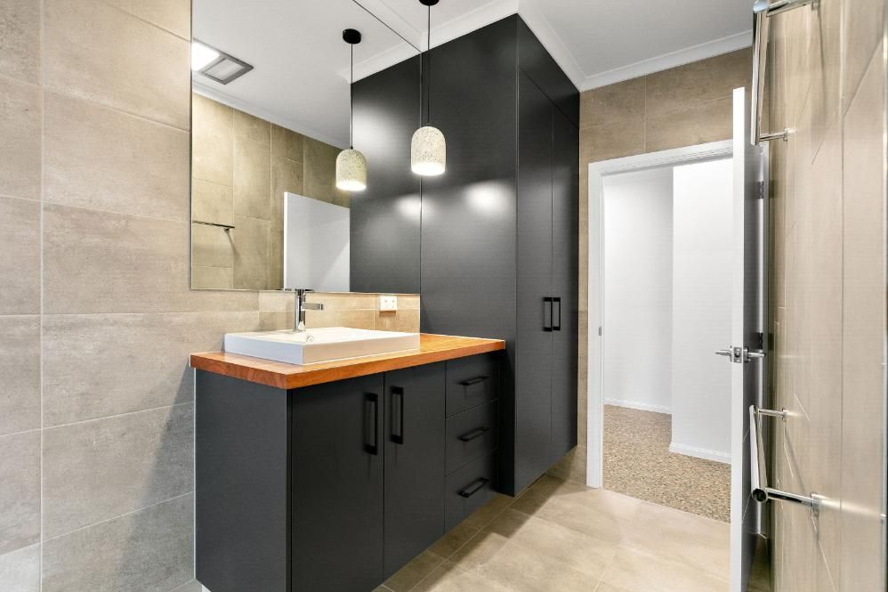 A Bathroom With a Sink, Mirror and Cabinets — Ashlee Jones Homes in Gordonvale, QLD