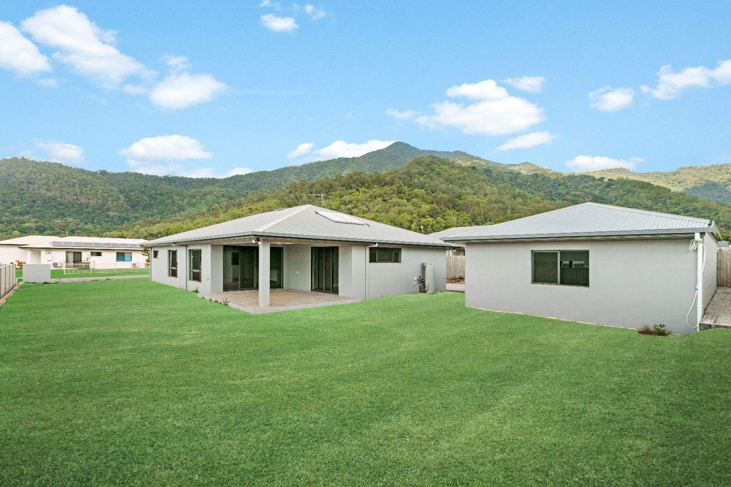 A couple of houses are sitting on top of a lush green hillside — Ashlee Jones Homes in Gordonvale, QLD
