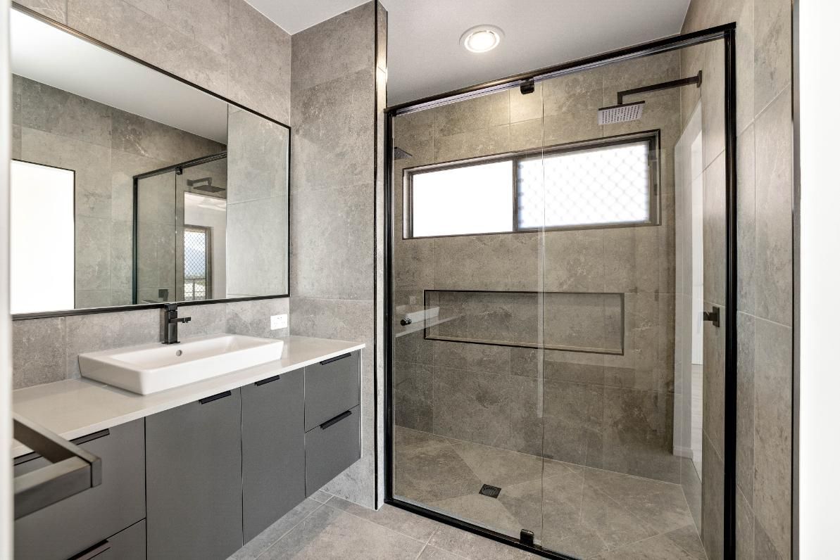A Bathroom With a Sink, Mirror, and Walk in Shower — Ashlee Jones Homes in Gordonvale, QLD