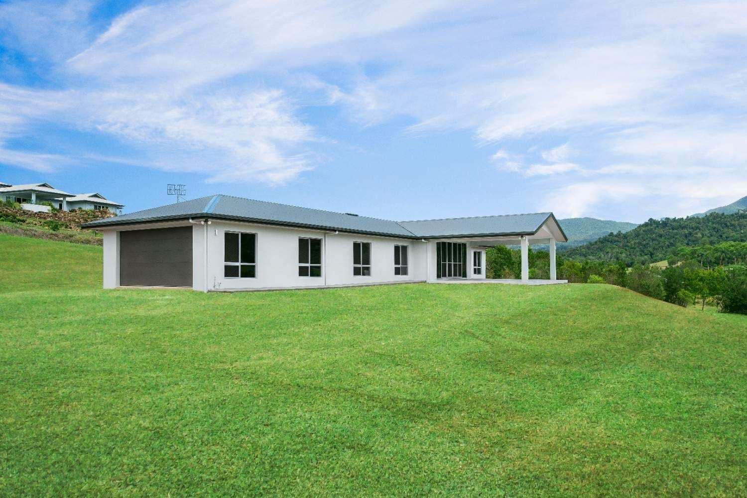 A Large White House is Sitting on Top of a Lush Green Hill — Ashlee Jones Homes in Gordonvale, QLD