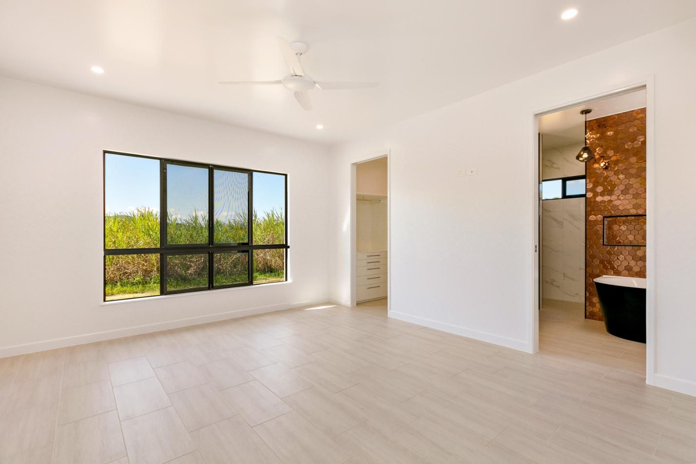 A Large Empty Room With a Ceiling Fan and Two Windows — Ashlee Jones Homes in Gordonvale, QLD